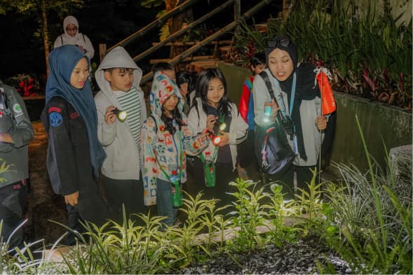 Sekelompok siswa berseragam duduk melingkar mendengarkan pendamping yang berdiri di depan tenda glamping berukuran besar