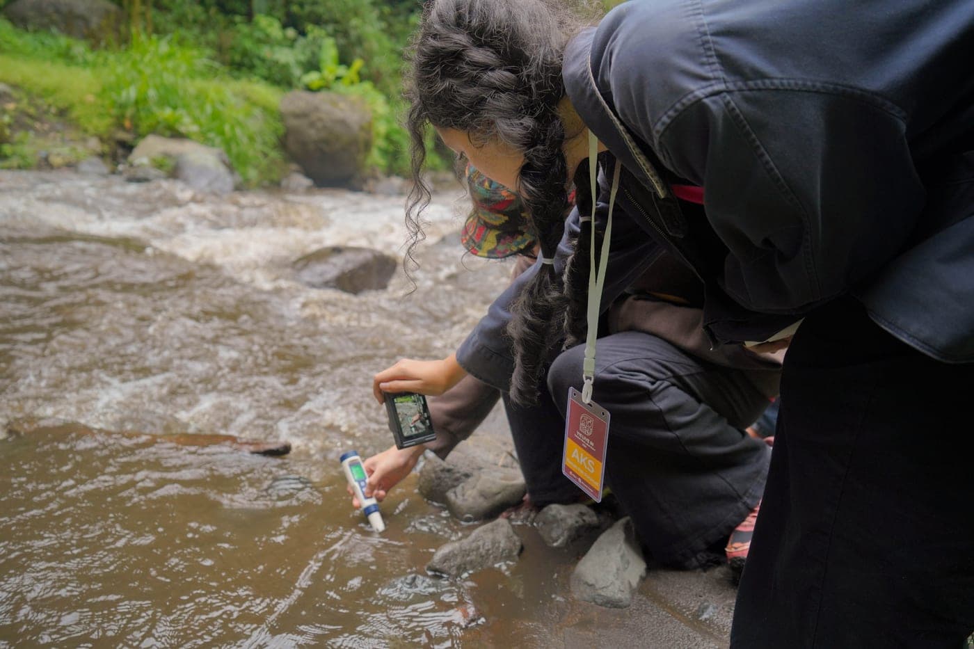 Seorang siswa berdiri di antara bebatuan sungai sambil memeriksa air dangkal di sekitarnya