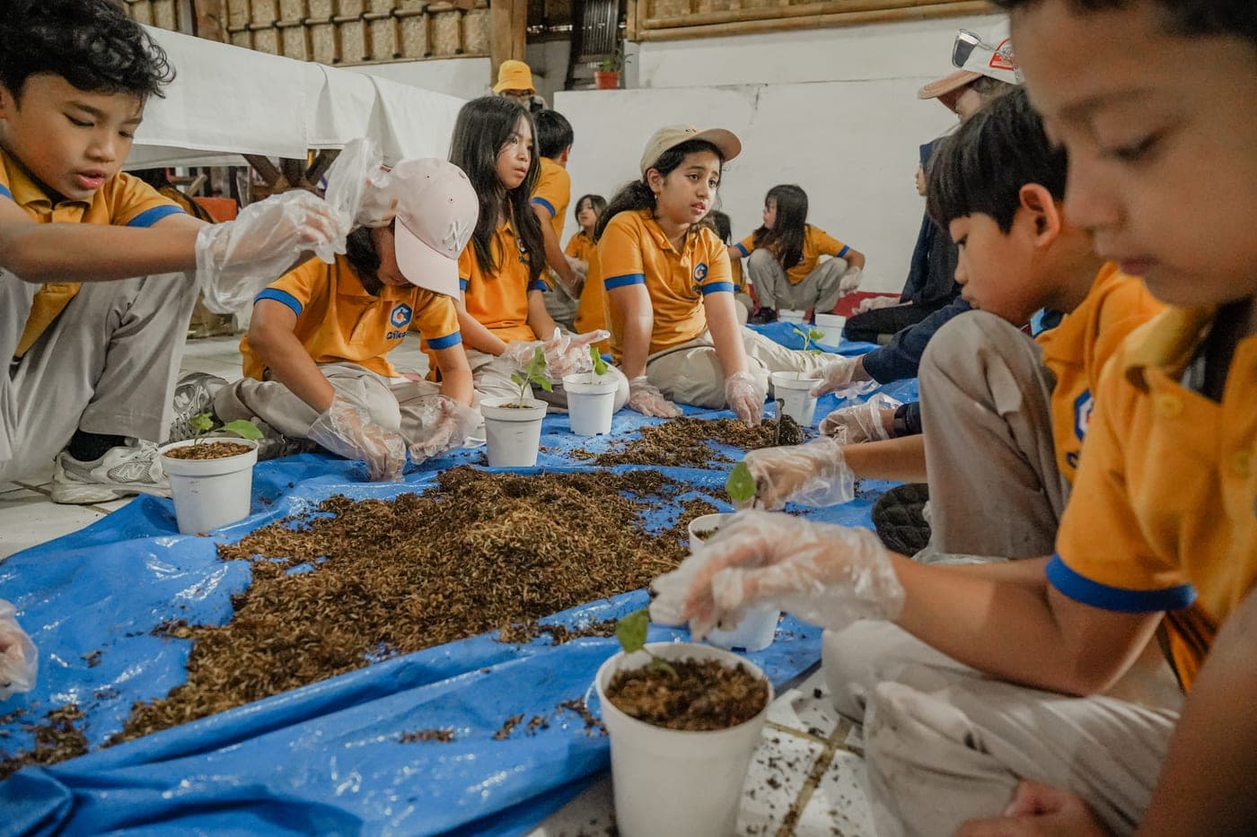Siswa berkaus kuning mencampur bahan organik dalam wadah pengomposan di area terbuka