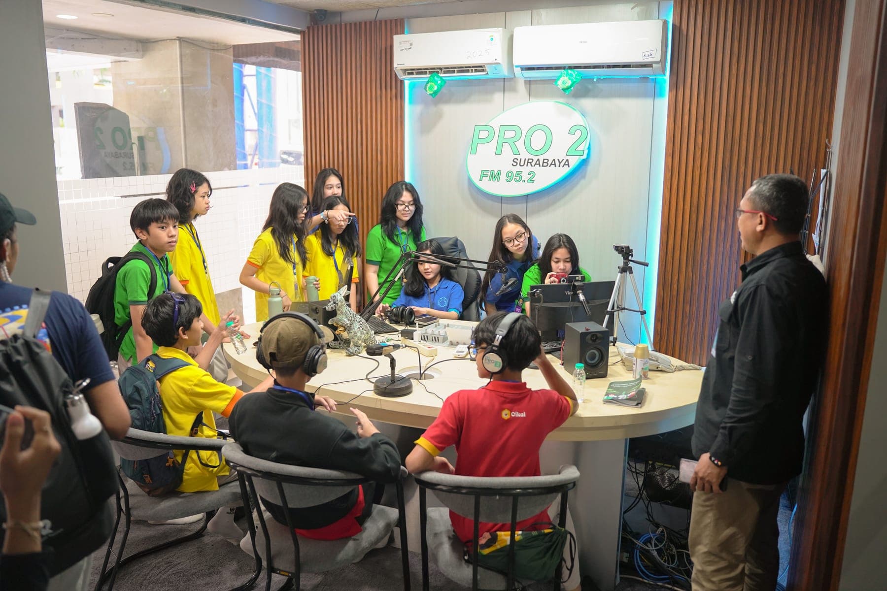 Dua siswa duduk di depan mikrofon studio siaran sambil mengenakan headphone didampingi penyiar