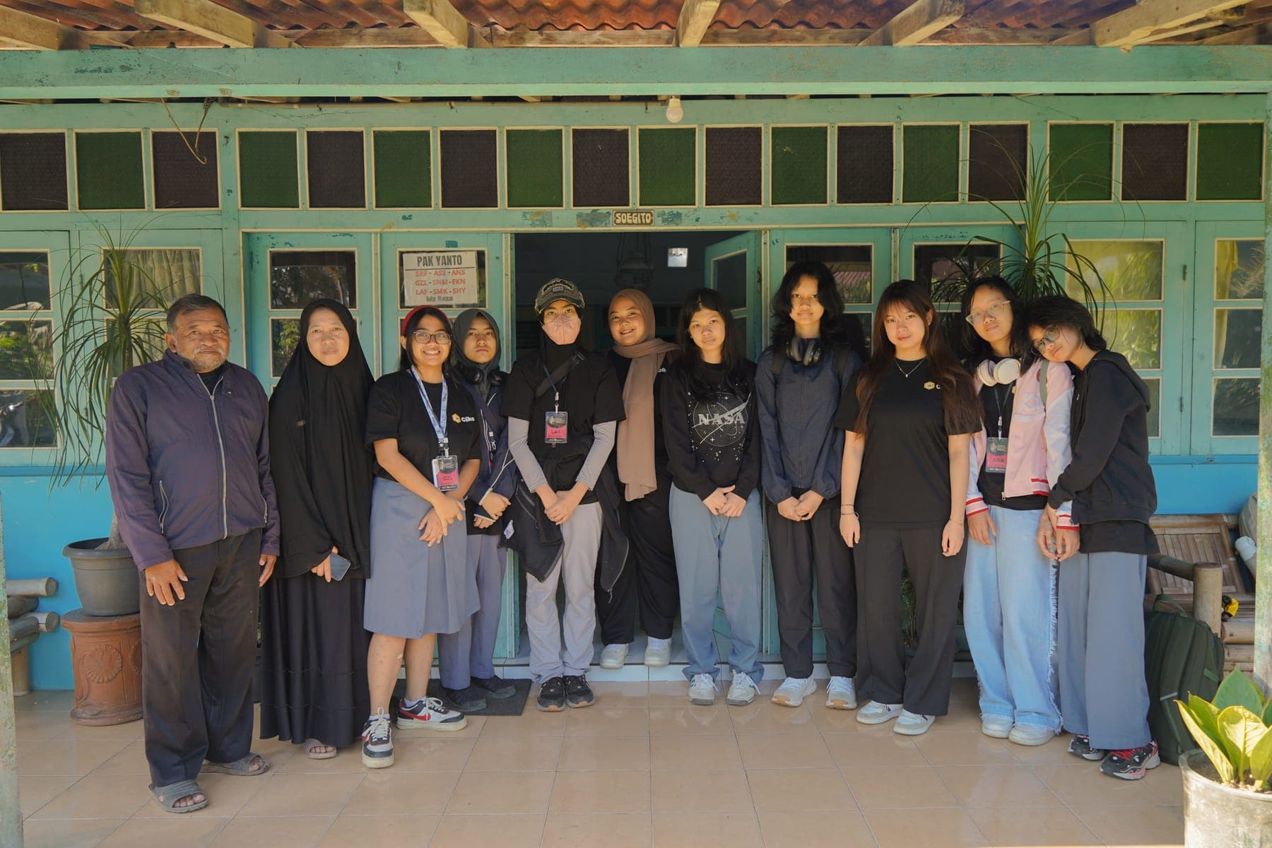 Foto bersama rombongan siswa dan warga desa berdiri berjajar di halaman terbuka pada sore hari