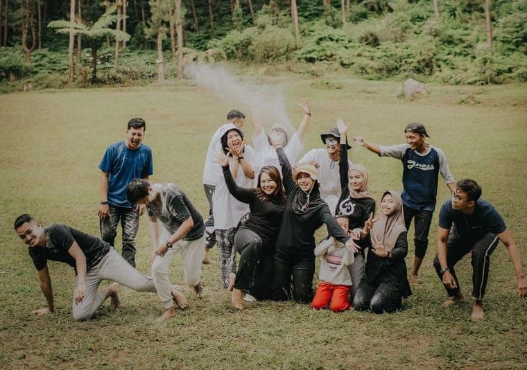Peserta outbound bermain fun games bersama di lapangan rumput yang dikelilingi pepohonan