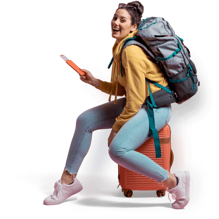 Wanita muda tersenyum sambil duduk di atas koper oranye, mengenakan ransel besar dan memegang tiket perjalanan
