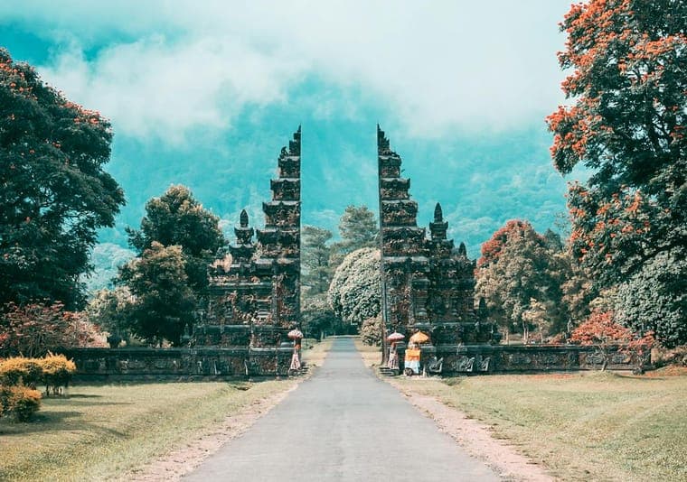 Gapura candi bentar khas Bali dengan jalan setapak menuju perbukitan berkabut